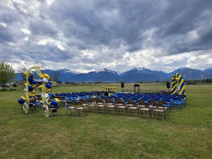 graduation ceremony set up outside on green grass and mountains in the background